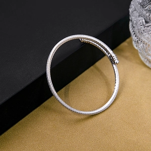 Macro detail of silver-colored twisted cable bangle with intricate texture on a modern surface