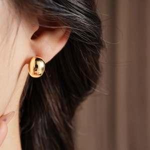 Close-up of a minimalist gold-plated hemispherical stud earring worn by a model