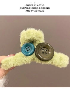 Close-up of green plush hair claw clip featuring large colorful decorative buttons