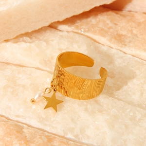 Macro detail of 18K gold plated wide band ring with pearl and star pendant charm