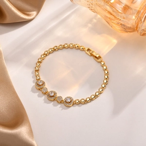 Detailaufnahme eines goldenen Armbands mit Zirkonia-Steinen auf champagnerfarbener Seide