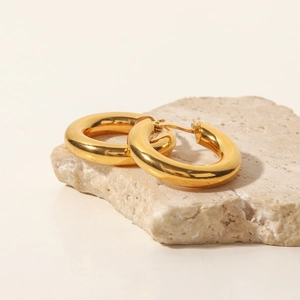 Detailed view of thick gold stainless steel hoop earrings on a textured stone surface