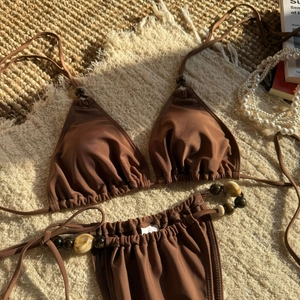 Detail of dark brown bikini ties with decorative amber textured beads on woven mat