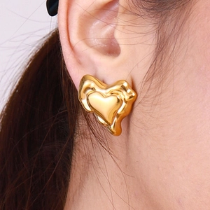 Gros plan d'une boucle d'oreille cœur dorée texturée portée sur le lobe de l'oreille