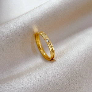 Close-up of a minimalist gold titanium ring with a single zircon on champagne silk fabric