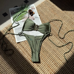 Detail eines olivgrünen Bikinis mit herzförmiger Metallschnalle und glänzendem Stoff