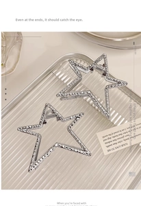 Detail view of two silver star-shaped metal hair claws with hammered texture on a tray