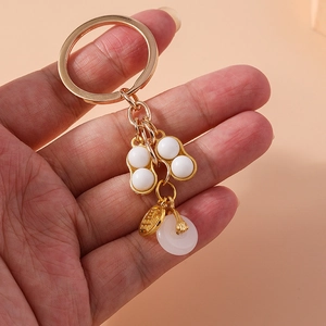 Golden keychain with faux jade peanuts and white peace buckle on warm orange background