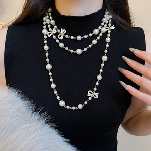 Close-up of layered pearl necklace with white enamel bow pendants on a black top
