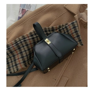 Minimalist black leather bag with gold clasp shown against a brown wool coat background