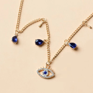 Collana dorata con ciondolo a forma di occhio blu e cristalli a goccia su sfondo beige