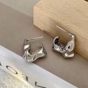 Detailed view of silver irregular liquid metal earrings on minimalist wooden props