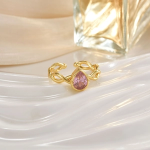 Detail of gold woven band ring featuring a pink pear-cut crystal on a reflective surface