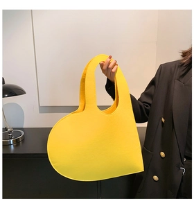 Detail of a bright yellow felt heart-shaped handbag held by a model in a modern setting