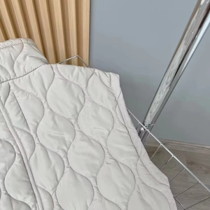 Detail of light grey quilted vest showing wave stitching and soft metallic fabric texture
