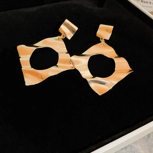 Close-up of golden geometric hollow drop earrings with hammered wave texture detail