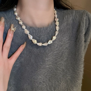 Close-up of model wearing irregular baroque pearl necklace over a soft grey sweater