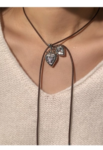 Close-up of heart pendant necklace with crown detail and brown cord on white knit sweater