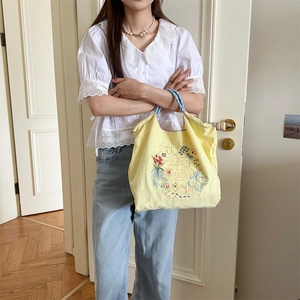 Détail du sac cabas en tissu jaune avec broderie colorée et anses tissées bleues