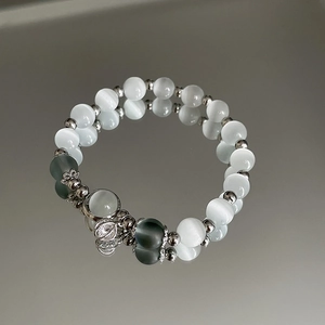 Detail eines Opal-Perlenarmbands mit Herzanhänger auf einer spiegelnden Oberfläche