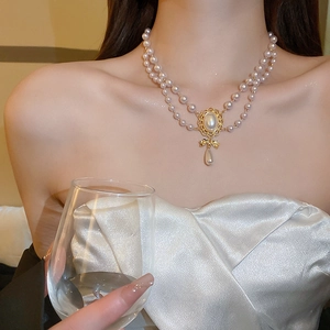 Double-layered pearl necklace with bow and teardrop pearl pendant on model
