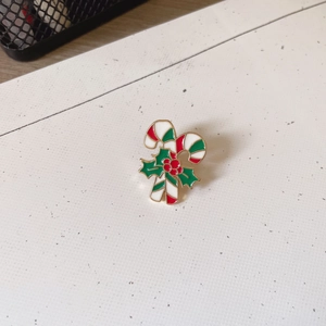 Detail of Christmas candy cane brooch with green holly leaves and red berries on white background