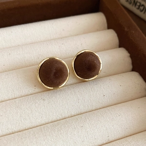 Detail of vintage gold-rimmed round earrings with dark brown flocking on a beige display