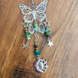 Detail of butterfly suncatcher with crystal beads and metal moon pendants on wood background