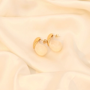 Detailed macro of gold drop earrings with creamy white resin stones on silk fabric