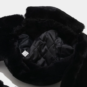 Detail view of black faux fur earflap hat showing quilted polyester lining and care label