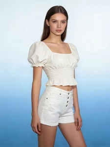 Detail of high waisted white denim shorts with four button fly and distressed ripped hem