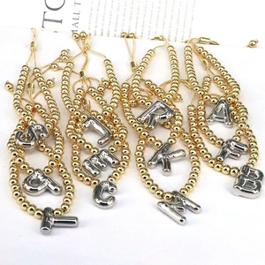 Detail of adjustable gold beaded bracelets with silver 3D alphabet charms on a white surface