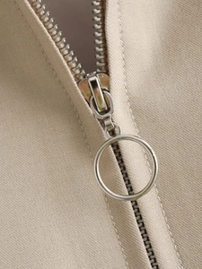Close-up of a circular metal zipper on a khaki twill jacket showing high-quality texture