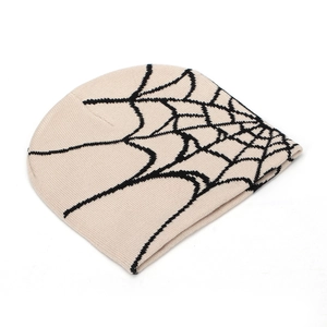 Close-up of cream knit beanie featuring a black spider web jacquard pattern detail