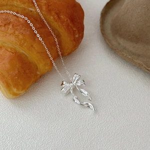 Elegant 925 sterling silver bow ribbon pendant necklace on a minimalist white desk