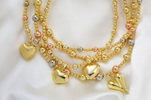 Close-up of tricolor beaded necklaces with heart pendants on elegant white silk background