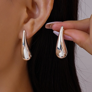 Close-up of minimalist silver water-drop earrings with a high-polished mirror finish on model
