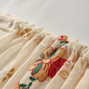 Close-up of elegant Christmas bell embroidery on white lace curtain with golden silk threads