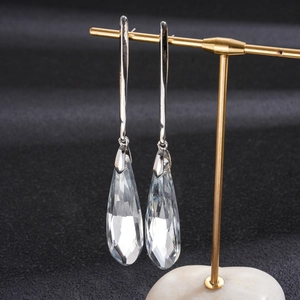 Macro shot of long silver earrings with clear teardrop crystal pendants on a gold stand