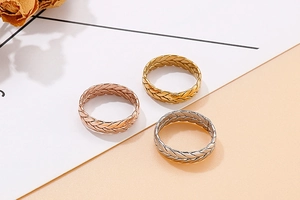 Dettaglio degli anelli con trama a spiga intrecciata nei colori oro rosa, oro e argento