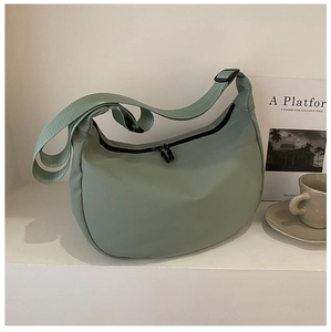 Close-up of a minimalist light green nylon crescent bag with adjustable wide strap and zipper