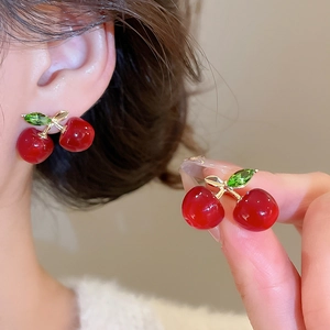 Detailed view of red resin cherry earrings with green crystals on a model ear