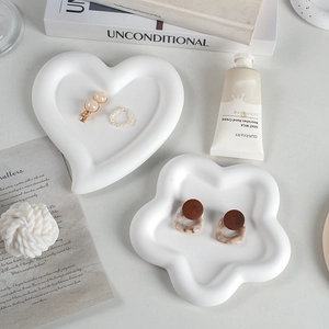 White heart and flower shaped ceramic jewelry trays displayed on a minimalist table