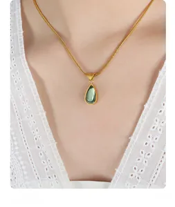 Close-up of gold snake chain with green teardrop pendant on white lace top