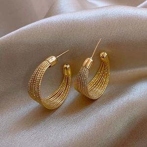 Macro shot of gold layered woven hoop earrings on elegant silk fabric background