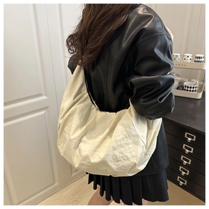 Rear view of cream large nylon dumpling bag on shoulder with casual pleated skirt outfit