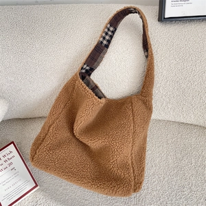 Detail of soft brown teddy fleece hobo bag with plaid strap lining on a white sofa