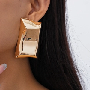 Close-up of oversized irregular gold rectangular metal earring worn on model's ear
