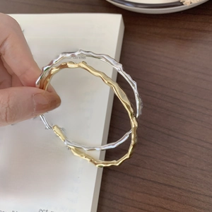 Close-up of minimalist S925 silver and gold wave bracelets on a vintage book page