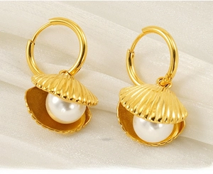 Macro view of gold shell earrings with pearl inlay on white silk fabric background